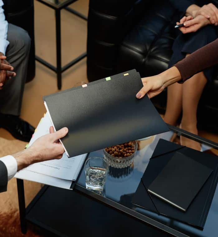 Top view closeup of business people handing binder with documents over coffee table during meeting in luxury office, copy space